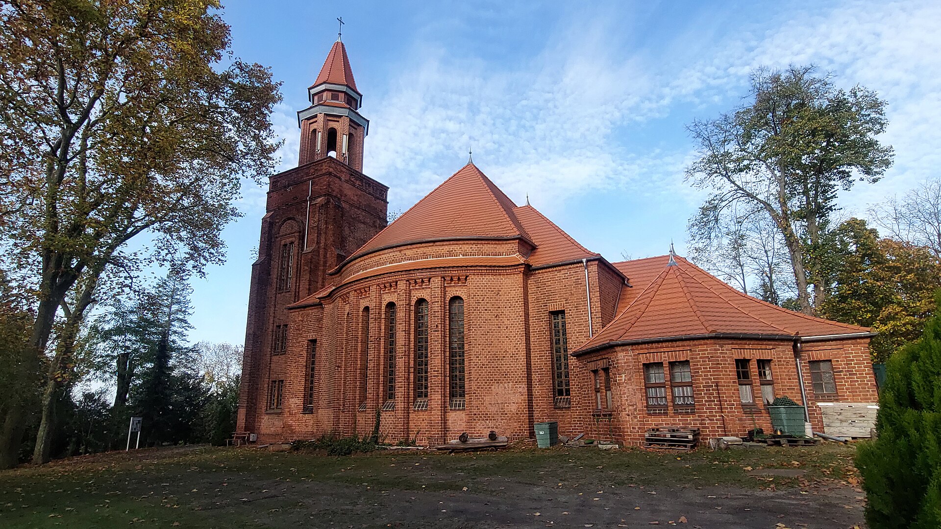 Eine rote Backsteinkirche mit einem hohen Glockenturm unter blauem Himmel.