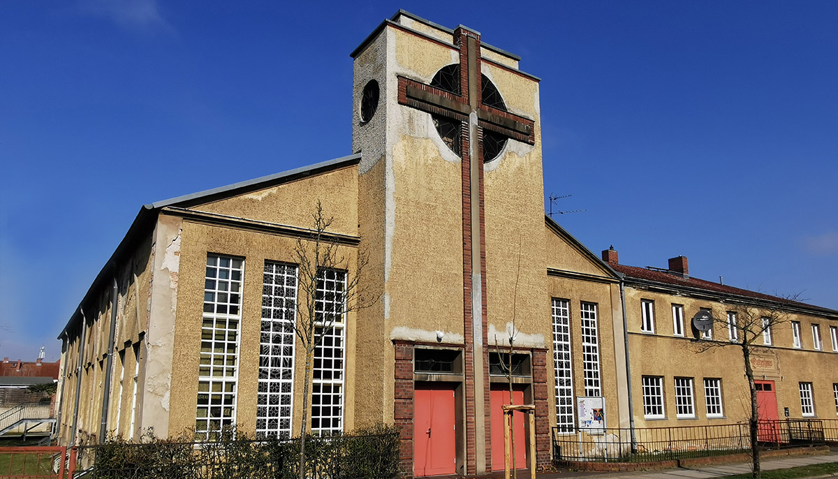Eine beige Kirche mit einem großen Backsteinkreuz auf der Fassade.