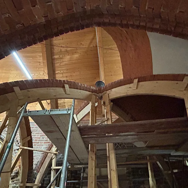 Ein neuer Backsteinbogen für das Kirchengewölbe wird mit einer Holzform gemauert. zwei